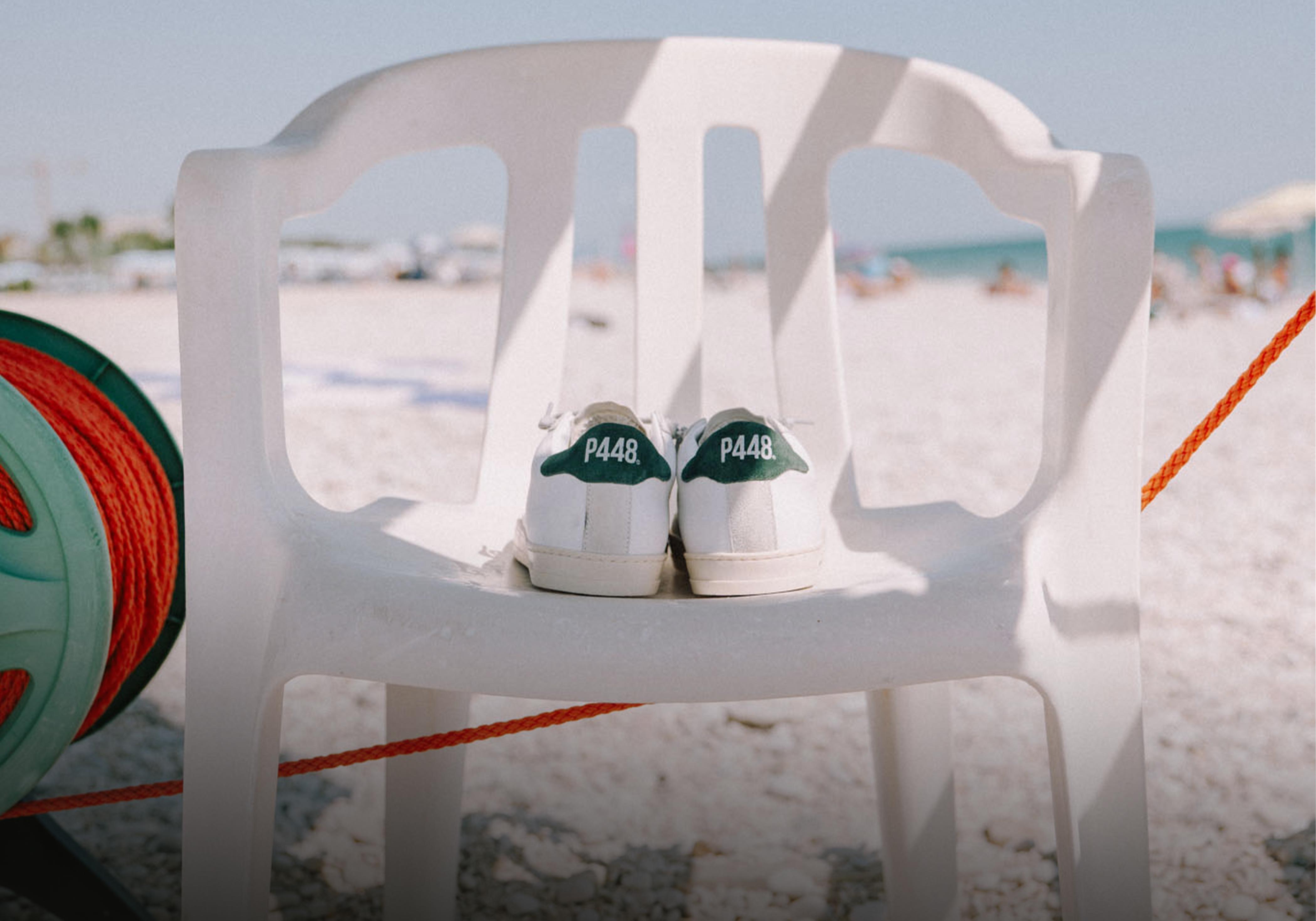 P448 white leather Sneakers with green heel tab on a white beach chair, summer Shoes